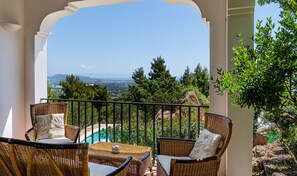Un balcon agrémenté de meubles en osier, avec vue sur une piscine et entouré de verdure.