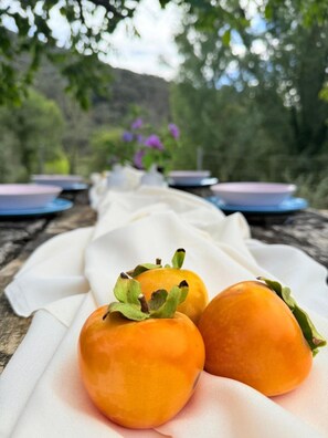 A table with a white cloth, three persimmons, and a blurred outdoor background.