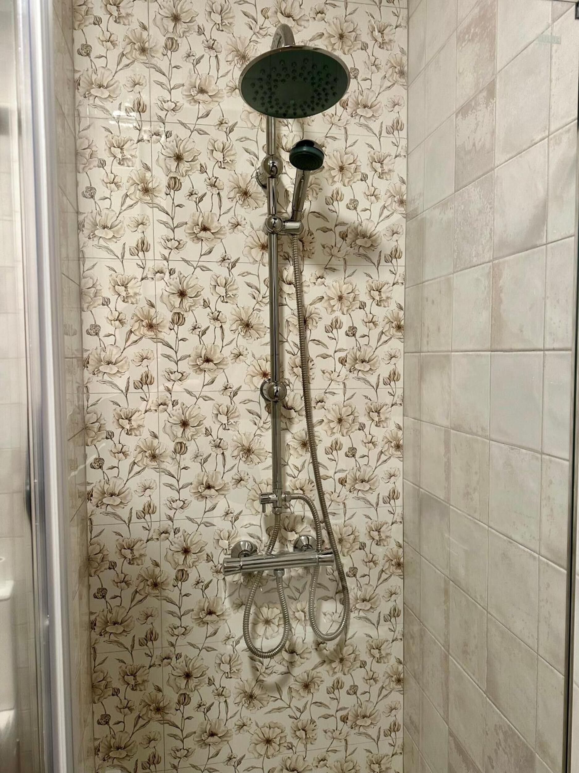 Una ducha con un estampado de baldosas florales, un cabezal de ducha manual y un accesorio de ducha manual.