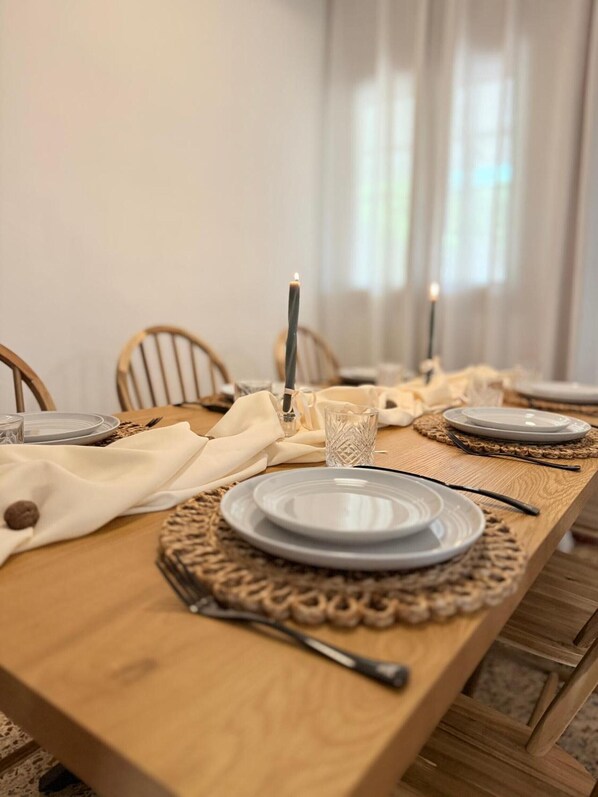 A dining table set with plates, cutlery, and candles, with chairs around it.