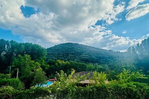 A mountainous landscape with a house surrounded by dense greenery and a clear sky.