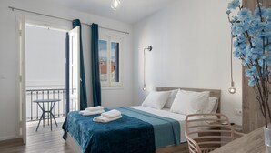 Un dormitorio con cama, mesa, silla y balcón, con vistas al exterior.