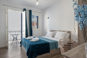 Ein Schlafzimmer mit Bett, Tisch, Stuhl und einem Balkon mit Blick ins Freie.