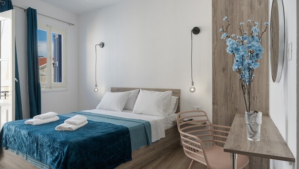 Un dormitorio con cama, un escritorio, una silla, un espejo y un florero con flores.