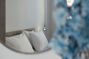 Ein Bett mit weißen Kissen und einem hölzernen Kopfteil, eine Pendelleuchte und ein unscharfes blaues Objekt im Vordergrund.