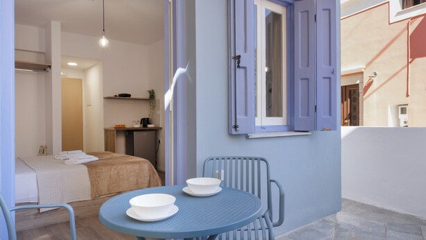 A room with a bed, a table with two bowls, a chair, and a window with open shutters. - Room 'Double  3' with Private Terrace, Wi-Fi and Air Conditioning (Ano Symi)
