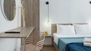 Et soveværelse med et træskrivebord, en stol, en seng med hvide sengetæger, en vægmonteret lampe og et spejl.