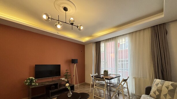 A modern living room with a flat-screen TV, a dining table with chairs, a sofa, and a ceiling light fixture. - Bright 2BR in Taksim Near Acıbadem Hospital (Istanbul)