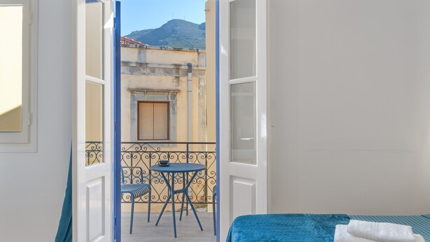 A room with a bed, a balcony with a table and chairs, and a view of a mountain. - Studio '11' with Private Balcony, Kitchenette, Wi-Fi and Air Conditioning (Ano Symi)