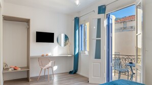 A bedroom with a bed, a desk, a chair, a TV, and a balcony with a chair. - Studio '11' with Private Balcony, Kitchenette, Wi-Fi and Air Conditioning (Ano Symi)