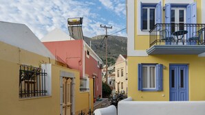 A narrow street with colorful buildings, a mountain in the background, and a clear sky. - Studio '11' with Private Balcony, Kitchenette, Wi-Fi and Air Conditioning (Ano Symi)