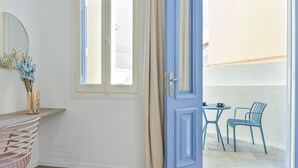 Een kamer met een houten bureau, een stoel, een spiegel, een blauwe deur en uitzicht op een terras.