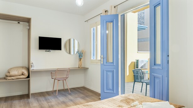 Een slaapkamer met een bed, een bureau, een stoel, een televisie en een badkamer die door een open deur zichtbaar is.