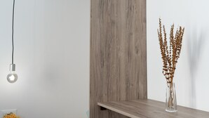 Ein Holzregal mit einer Vase aus getrockneten Pflanzen, einer Glühbirne und einem Kranz.