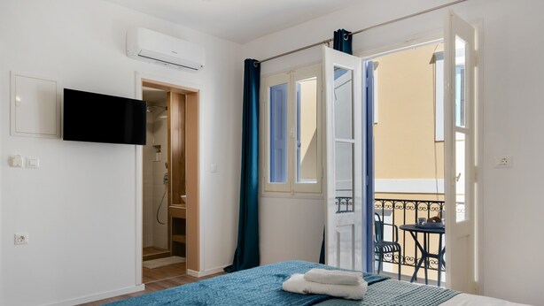 Ein Hotelzimmer mit Bett, einem an der Wand befestigten Fernseher, einer Duschkabine und einem Balkon mit Tisch und Stühlen.