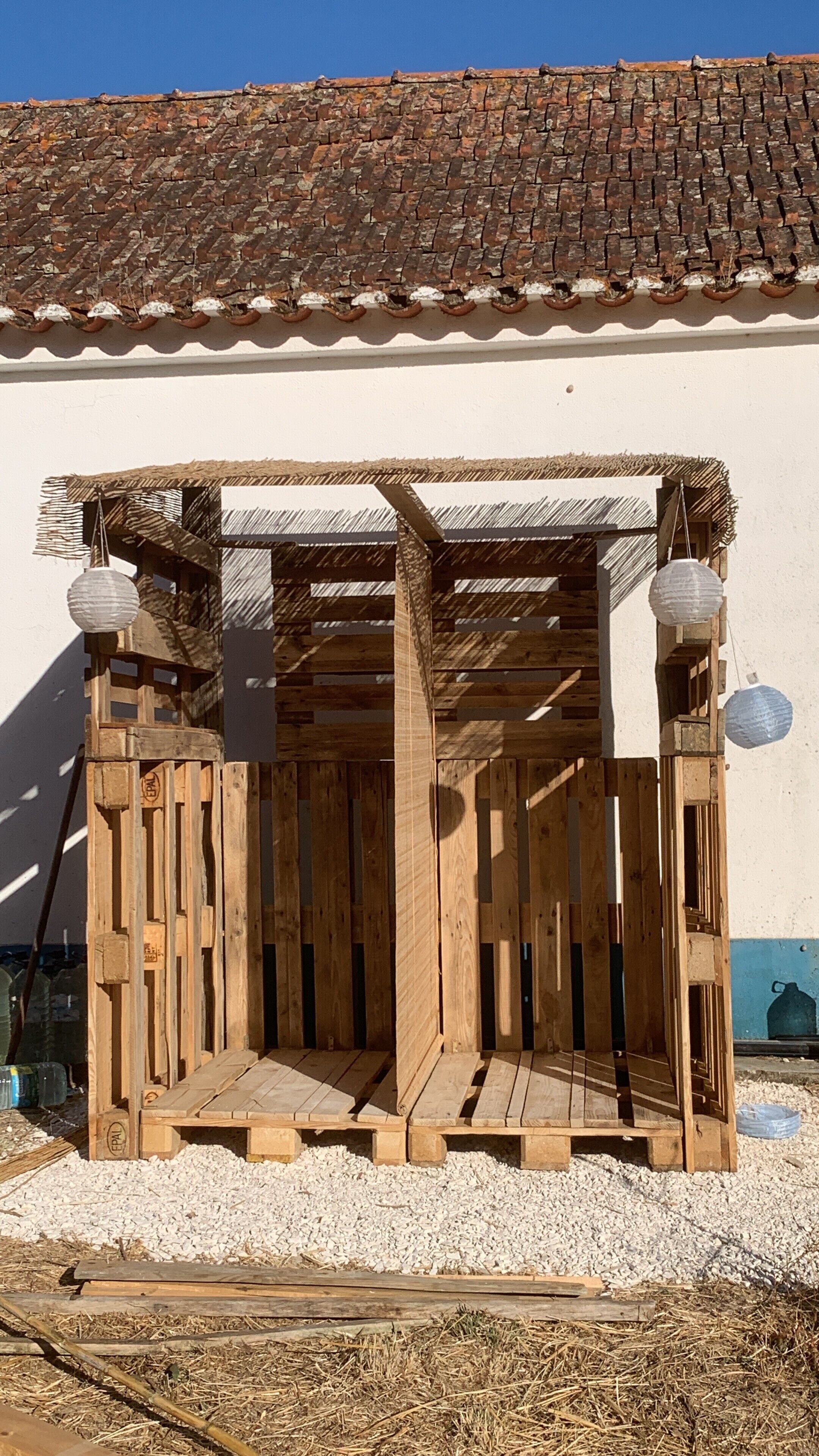 Una struttura in legno con tetto di paglia, un muro bianco e un tetto a tegole sullo sfondo.