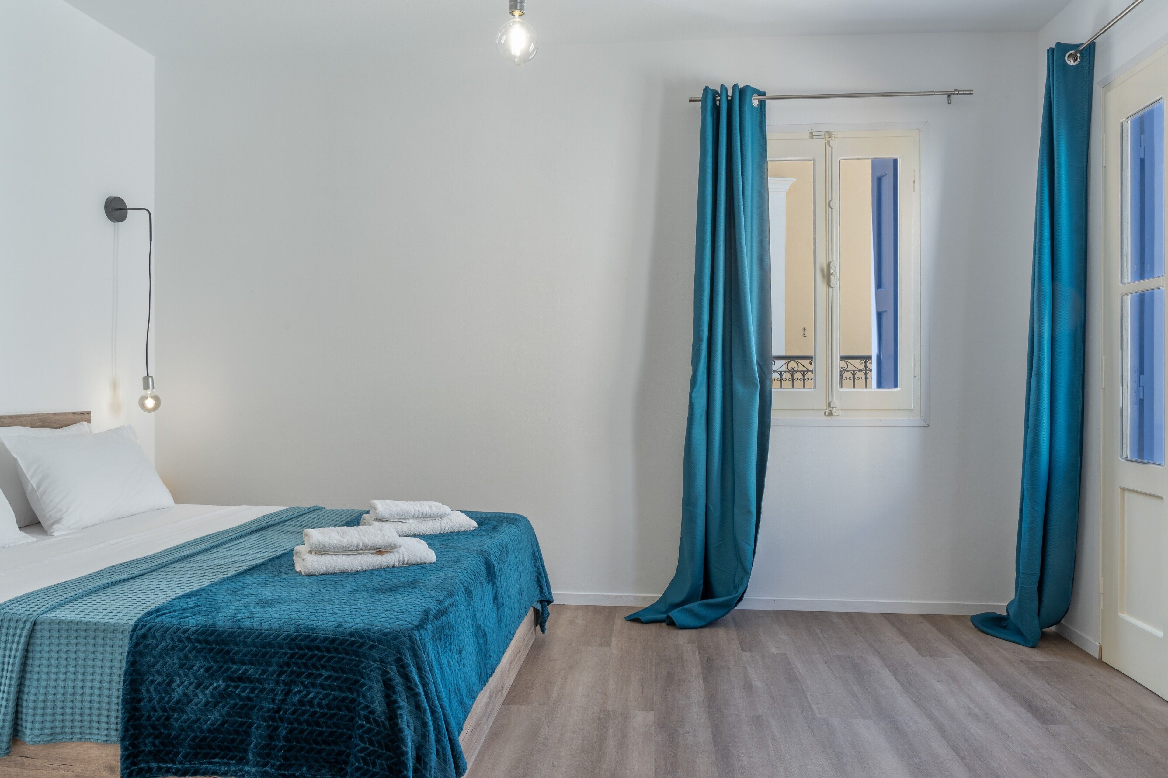 Een slaapkamer met een bed, een raam met gordijnen, een bedlamp en een houten vloer.