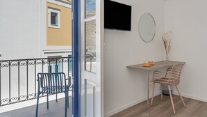 Un balcone con una sedia e un tavolo, una TV montata a parete e una finestra con vista su un edificio.