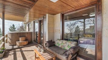 Een overdekt terras met een houten plafond, een bank met kussens, een houten tafel met kaarsen en een jacuzzi.