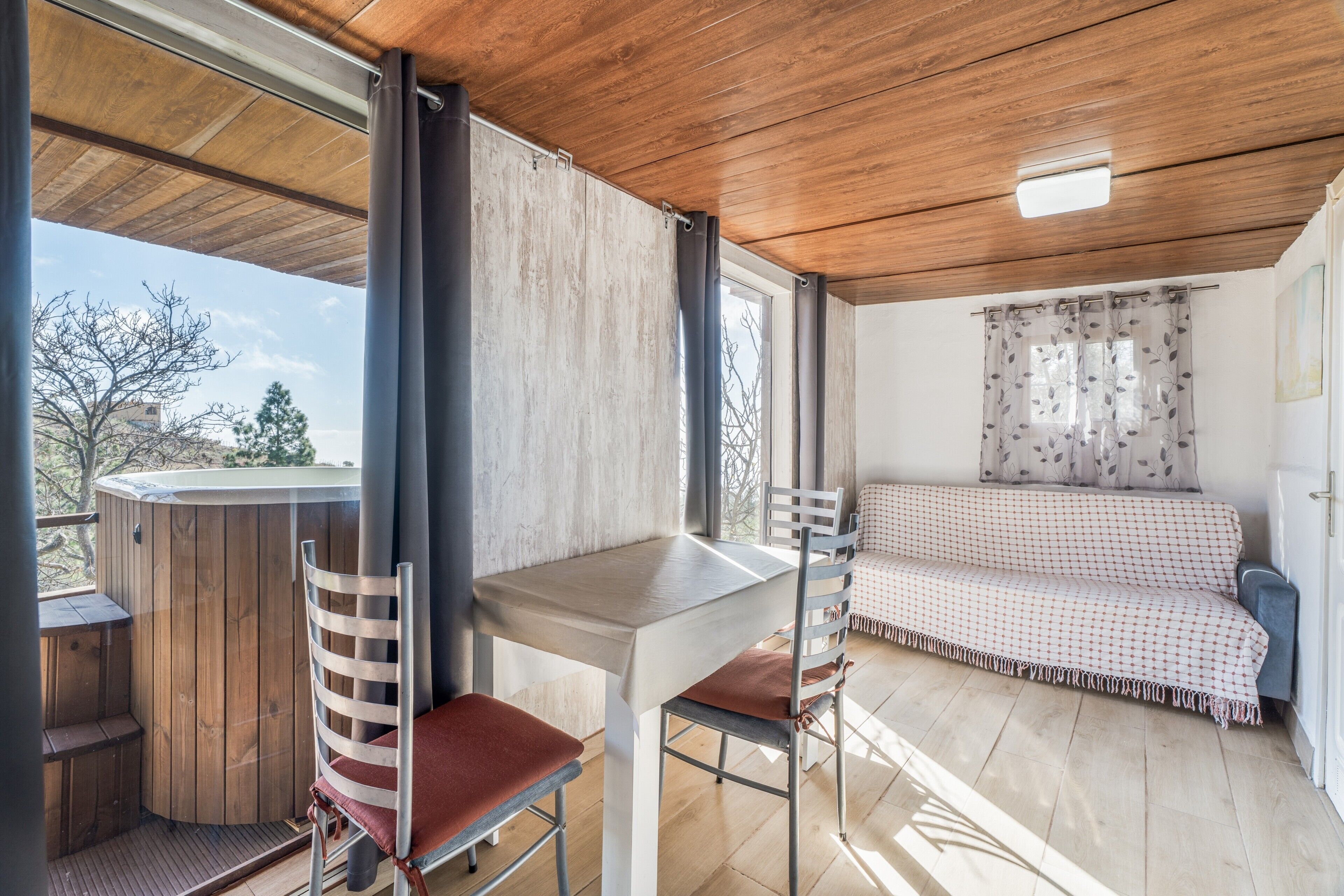 Una stanza con soffitto in legno, un tavolo con sedie, un divano e vista sull'esterno.