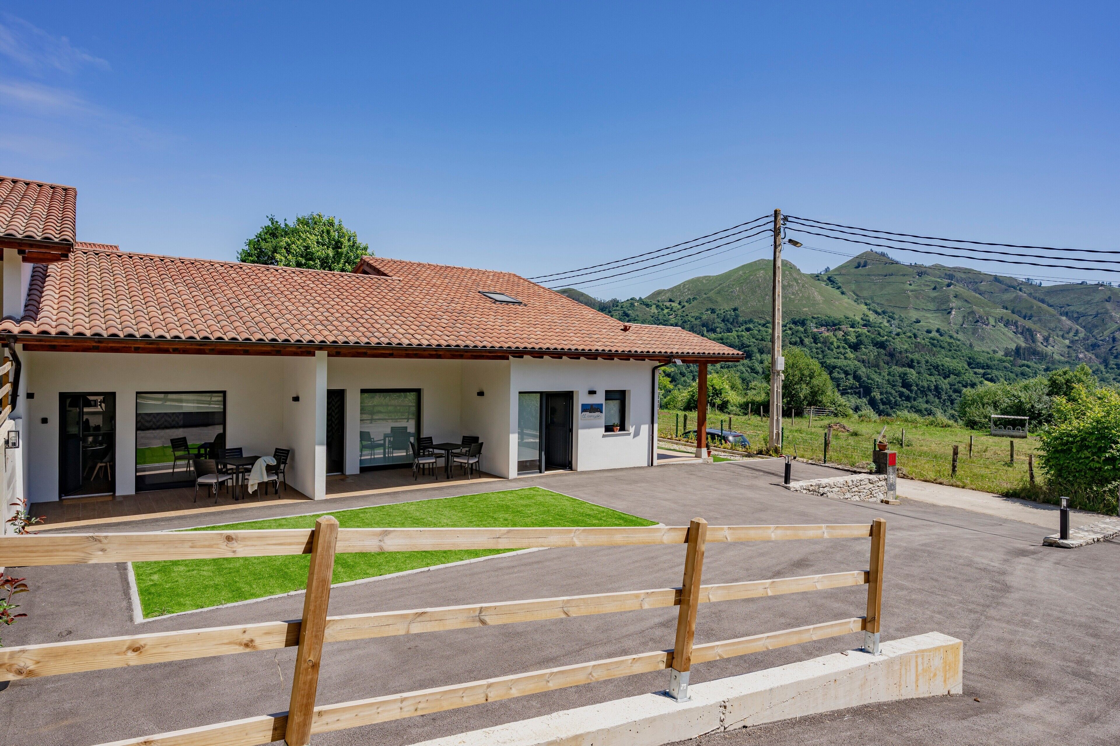 A modern building with a tiled roof, a covered patio, and a view of green hills.
