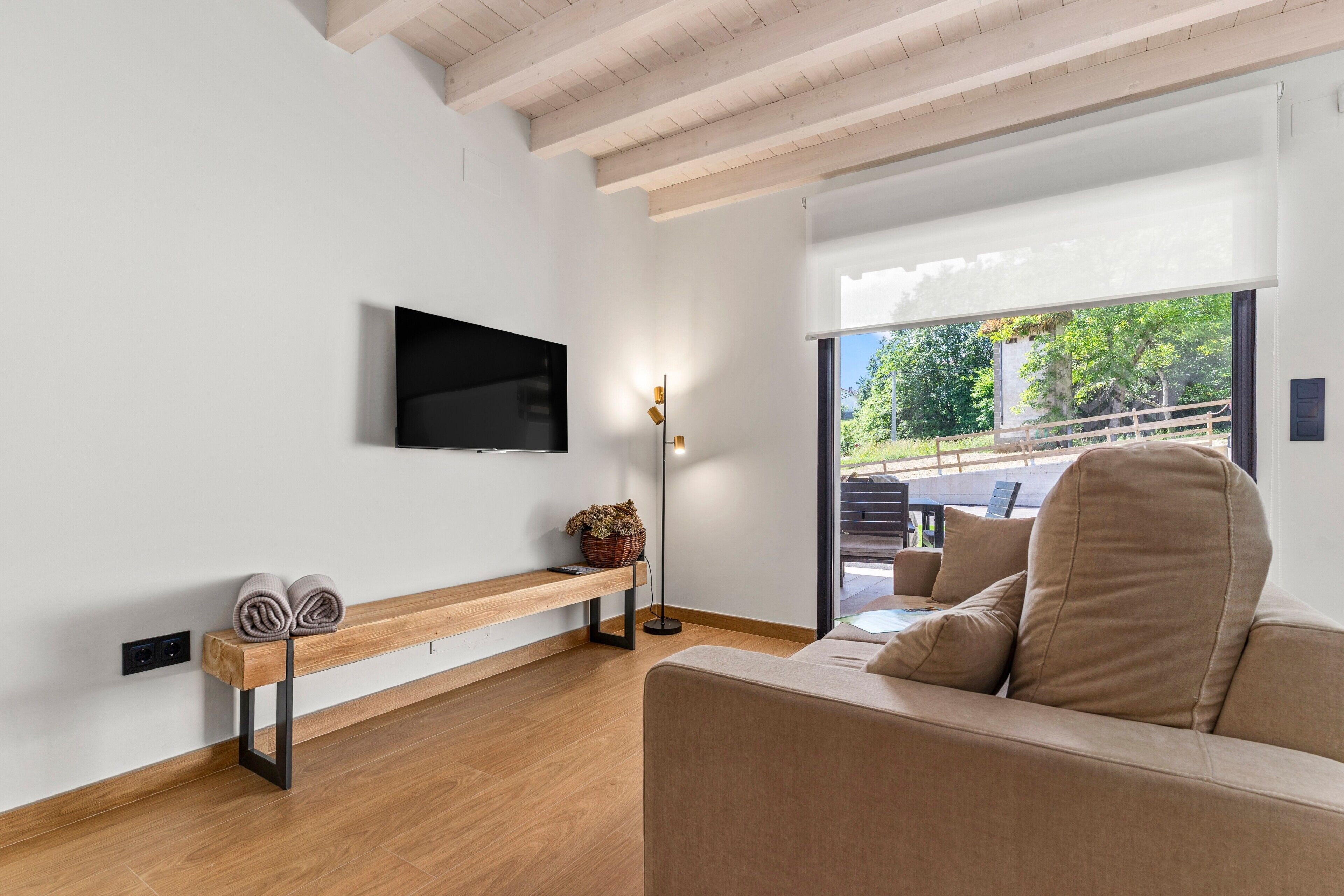 Una sala de estar moderna con un televisor de pantalla plana, un banco con toallas, un sofá y un ventanal con vistas a una terraza exterior.