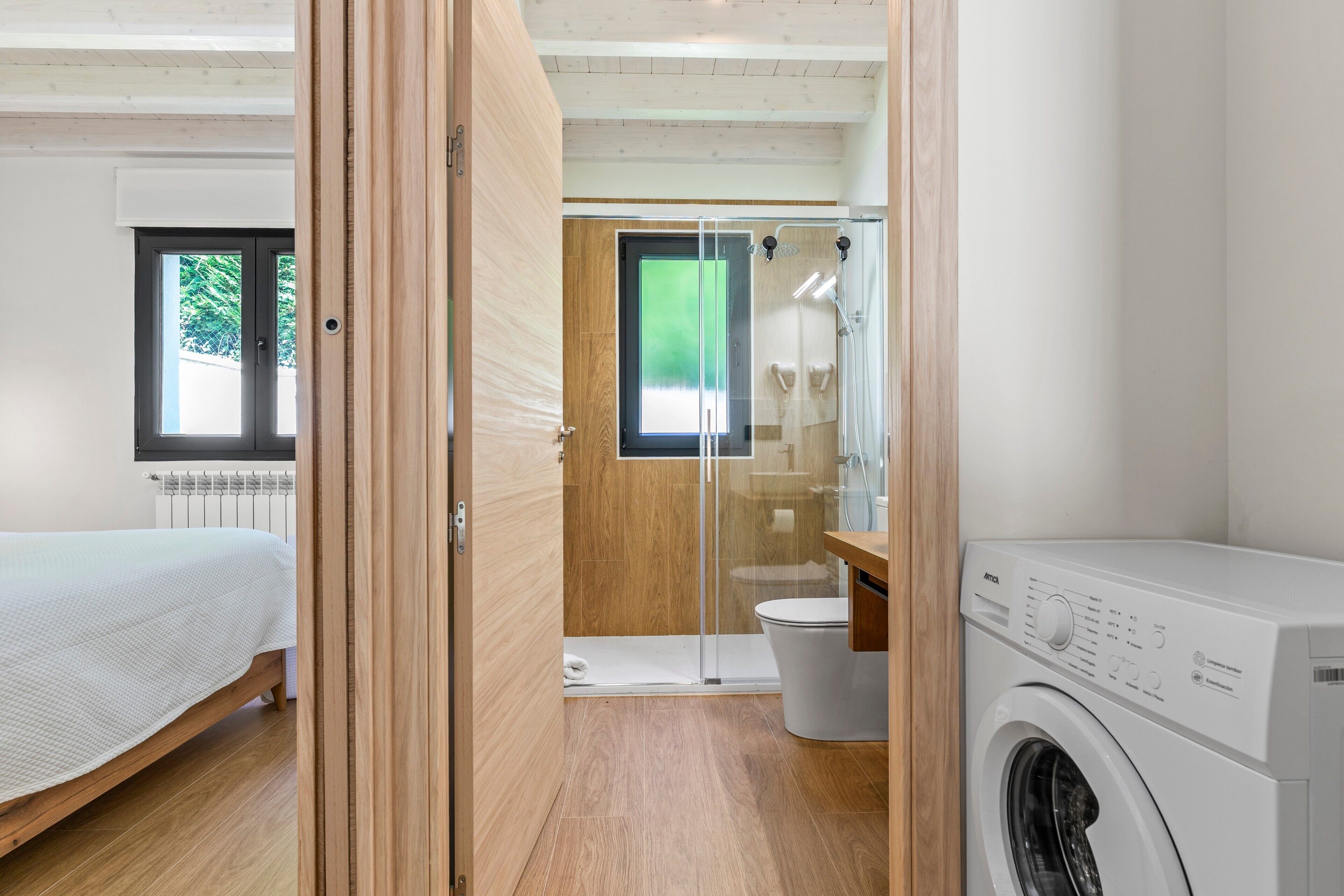 A bedroom with a bed, a wooden door, a glass shower enclosure, and a washing machine.