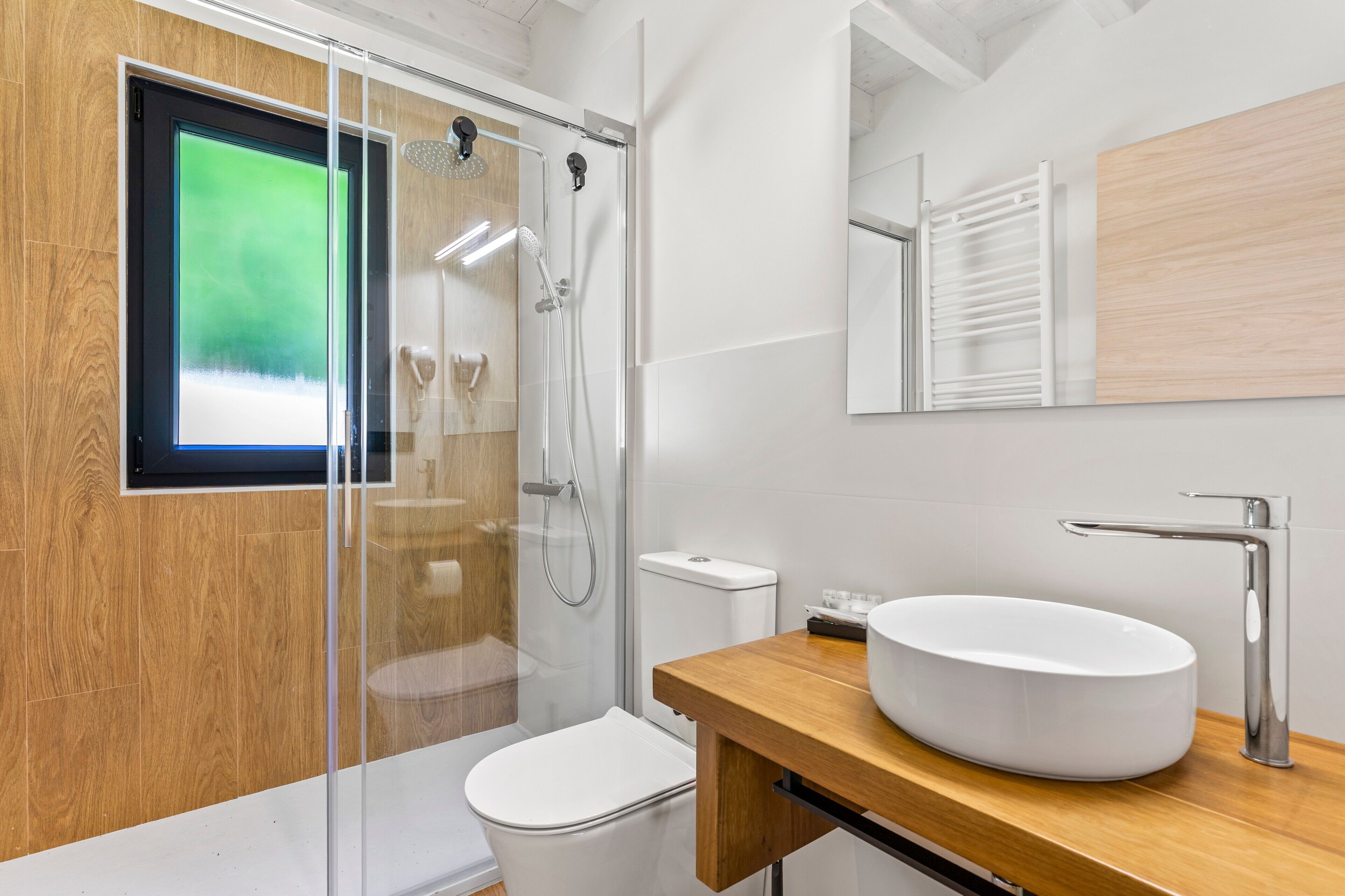 A modern bathroom with a glass shower enclosure, a white toilet, a wooden vanity with a large sink, and a mirror above the vanity.