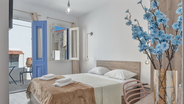Een slaapkamer met een bed, een houten hoofdbord, een nachtkastje, een vaas met bloemen en uitzicht op het omliggende landschap.
