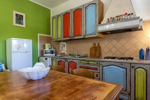 A kitchen with a wooden table, cabinets, a microwave, and a refrigerator. - Casa Marina Lu Tuvaraggiu: private terrace, Wi-Fi and air conditioning (Sorso)