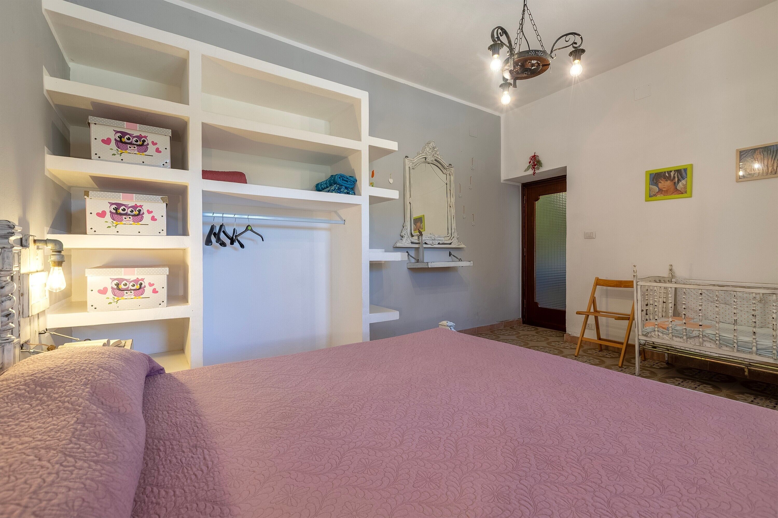 A bedroom with a large bed, white shelving unit, a mirror, and a crib.