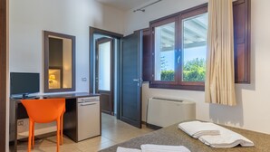 A bedroom with a bed, a desk, a chair, a window with curtains, and a view of greenery outside.