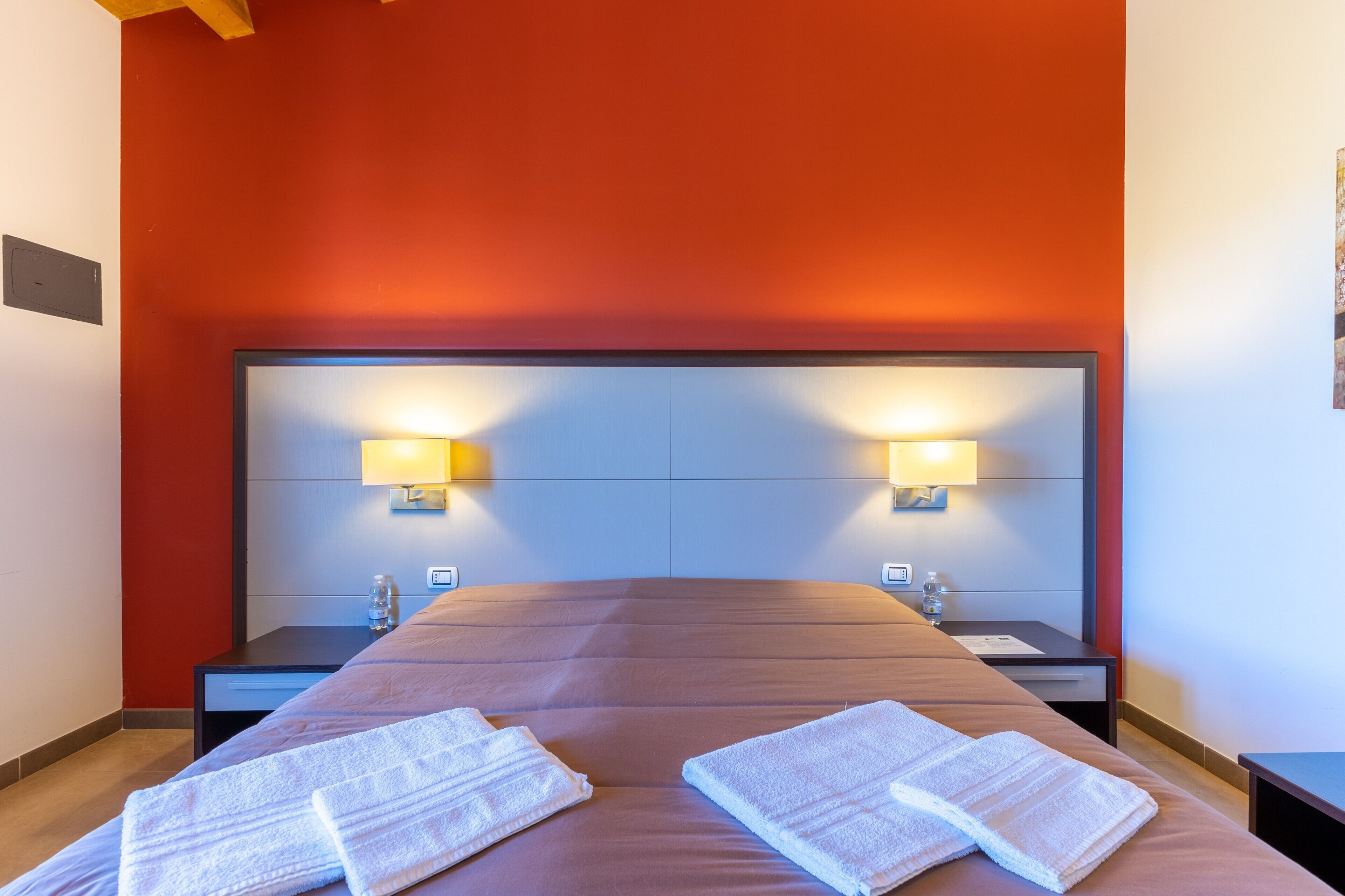 Habitación de hotel con una cama grande, dos mesitas de noche y lámparas fijadas a la pared.