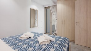 A modern hotel room with a large bed, a wardrobe, a mirror, and a sliding glass door to a balcony. - Elva Creta Beach Apartment with Sea View, Wi-Fi, and Air Conditioning (Palaiokastro)