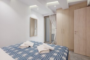 A modern hotel room with a large bed, a wardrobe, a mirror, and a sliding glass door to a balcony. - Elva Creta Beach Apartment with Sea View, Wi-Fi, and Air Conditioning (Palaiokastro)