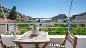 A balcony with a table and chairs, overlooking a coastal area with buildings and a hill. - Elva Creta Beach Apartment with Sea View, Wi-Fi, and Air Conditioning (Palaiokastro)
