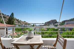 A balcony with a table and chairs, overlooking a coastal area with buildings and a hill. - Elva Creta Beach Apartment with Sea View, Wi-Fi, and Air Conditioning (Palaiokastro)