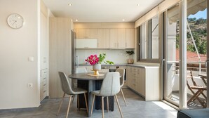 A modern kitchen with a dining table, chairs, and a vase of flowers. - Elva Creta Beach Apartment with Sea View, Wi-Fi, and Air Conditioning (Palaiokastro)