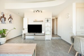 A modern living room with a flat-screen TV, a dining area with a table and chairs, and a staircase leading to another level. - Elva Creta Beach Apartment with Sea View, Wi-Fi, and Air Conditioning (Palaiokastro)