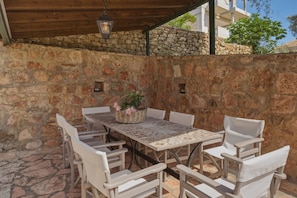Eine Terrasse im Freien mit einer Steinmauer, einem Tisch mit Stühlen und einer hängenden Leuchte.