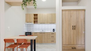 A kitchen with wooden cabinets, a white tiled backsplash, a dining table with chairs, and a wooden wardrobe. - Studio Apartment '6' with Shared Garden, Wi-Fi and Air Conditioning (Syvota)