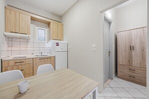 Eine Küche mit Holzausstattung, einer weißen Arbeitsplatte, einer Sp üle und einem Kühlschrank. Ein Esstisch mit einer weißen Tasse darauf.