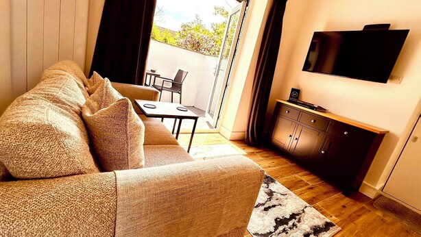 Una sala de estar con un sofá, un televisor de pantalla plana, una mesa de comedor y un ventanal corredero que da a un espacio exterior.