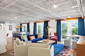 Un salon spacieux avec un plafond haut, un coin repas et de grandes fenêtres ornées de rideaux bleus.