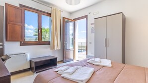 A bedroom with a bed, a desk, a wardrobe, and a sliding glass door leading to a balcony.