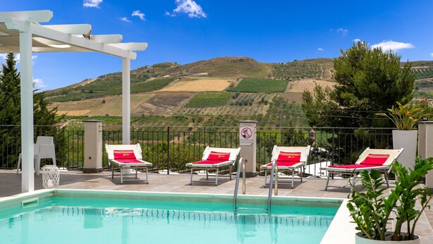 A pool with lounge chairs and a pergola, overlooking a hilly landscape.
