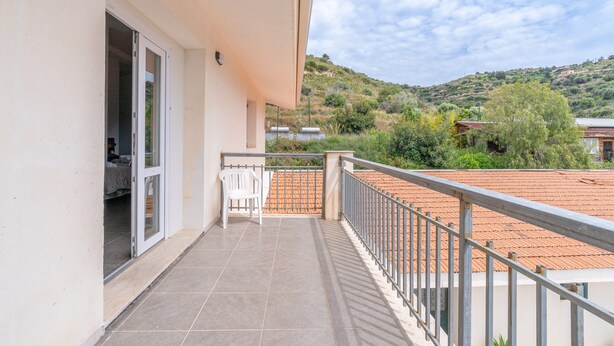 Un balcon avec une chaise, une porte-fenêtre coulissante et une vue sur un paysage vallonné.
