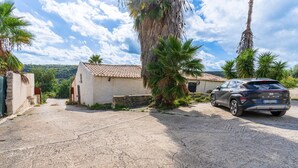 Un quartier résidentiel avec une voiture garée, une maison avec un toit en tuiles et des palmiers.
