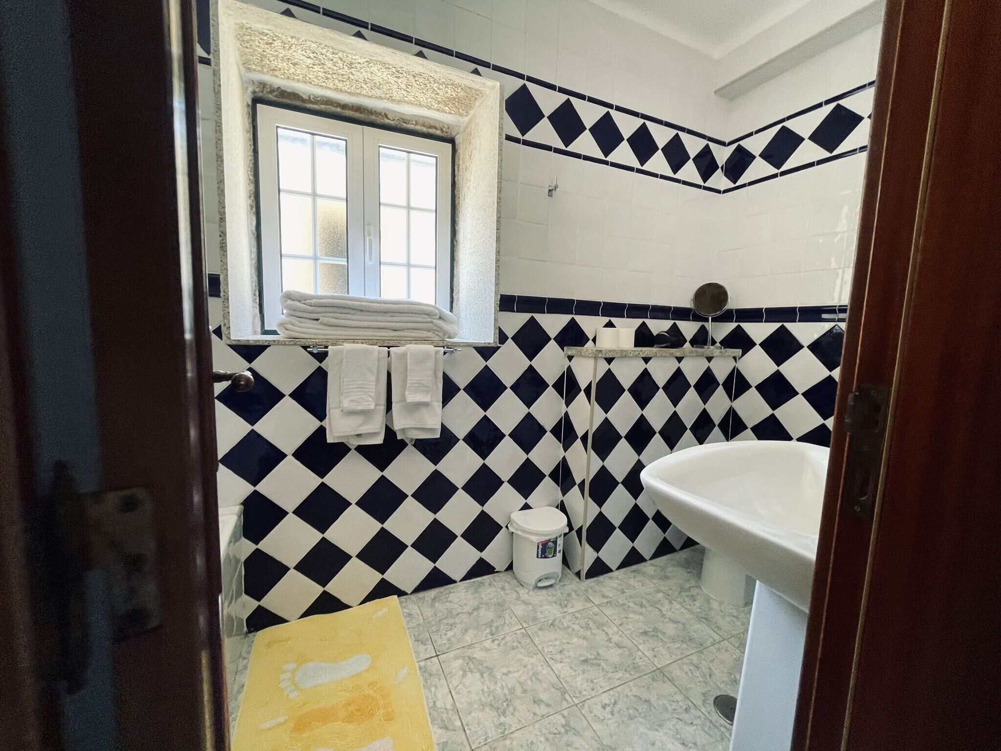 A bathroom with a checkered tile wall, a window, a sink, and a towel rack.
