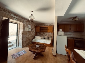 Eine kleine Küche mit Essbereich, Steinwänden, einem Bett mit Blick und einem Kühlschrank.